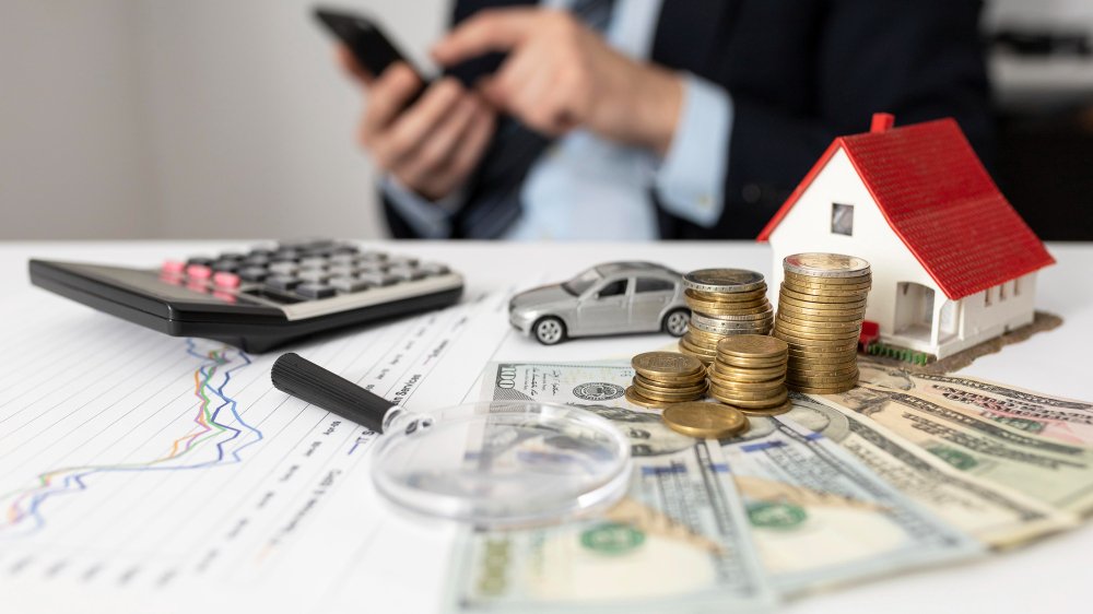 Casa, vehículo y monedas sobre un escritorio con calculadora, símbolo de crédito para tus proyectos